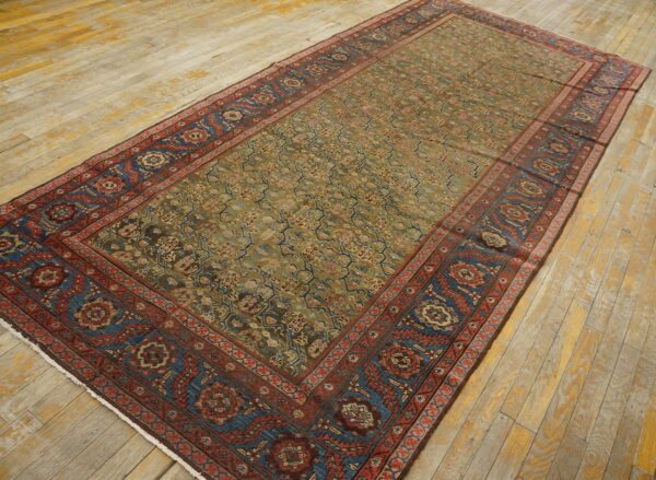 Traditional low-pile rug with a muted olive field and contrasting red and blue patterned borders on worn wood planks.