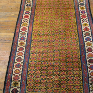 Mustard runner rug with repeating red and blue patterns, bordered by multi-colored shapes, on wood flooring.