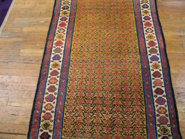 Mustard runner rug with repeating red and blue patterns, bordered by multi-colored shapes, on wood flooring.