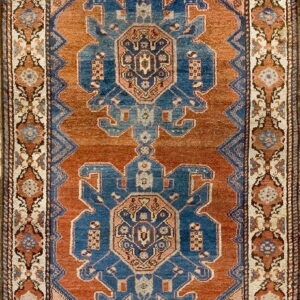 A traditional rug with two large blue geometric medallions centered on a rust-colored field.