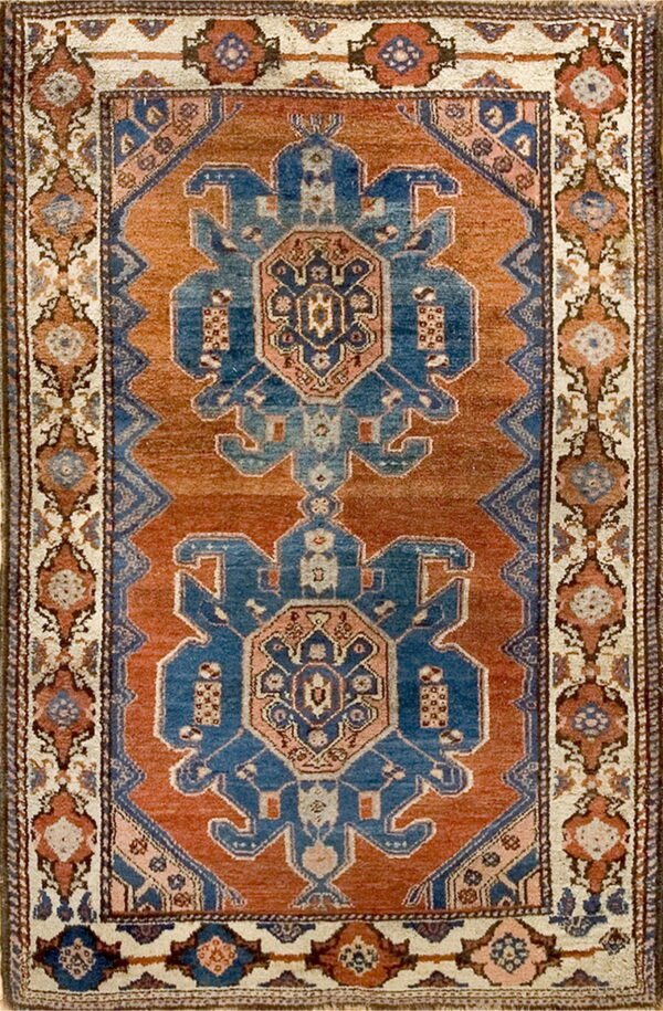 A traditional rug with two large blue geometric medallions centered on a rust-colored field.