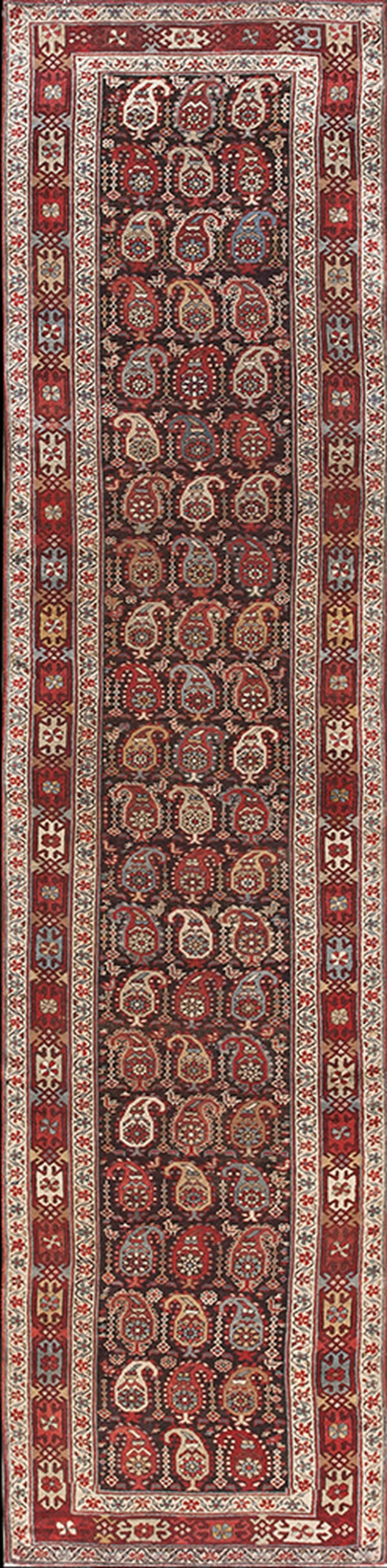 A narrow runner rug with a dark field and repeating red, cream, and blue stylized paisley motifs.