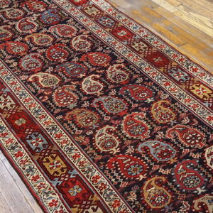 Red and blue paisley runner rug with multiple borders lying on rustic light wood planks.