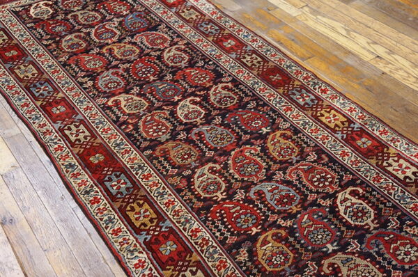 Red and blue paisley runner rug with multiple borders lying on rustic light wood planks.