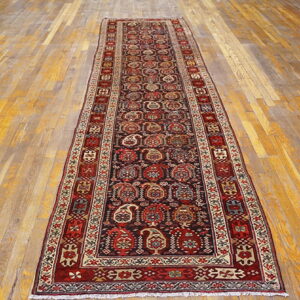 Traditional red, black, and cream runner rug with repeating designs placed on distressed wood flooring.