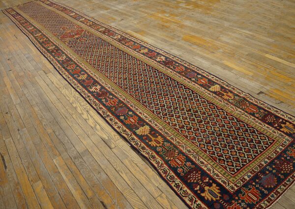 Navy and red geometric runner rug with wide borders is displayed on rustic light wood flooring.