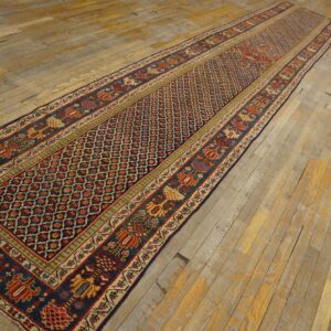 Dark blue runner rug with red geometric field and stylized motifs laid across wide, distressed wood planks.