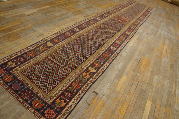 Dark blue runner rug with red geometric field and stylized motifs laid across wide, distressed wood planks.