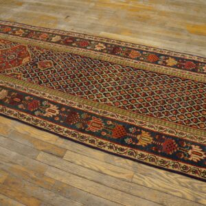 Low-pile geometric runner rug in red, dark blue, and cream on a light-colored, rustic hardwood floor.