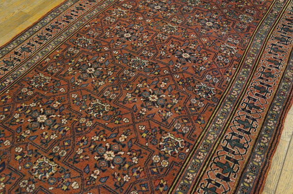 Burnt orange patterned runner rug with navy and cream motifs lying on light wood flooring.