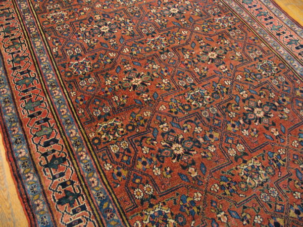 Rust rug featuring a dense floral geometric pattern in blue, cream, and yellow on wood floor.
