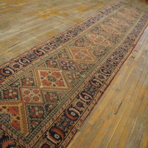 Multi-colored geometric runner rug featuring navy, rust, and tan diamonds on aged wood flooring.