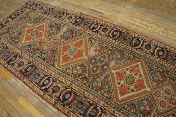 Distressed runner rug with blue and red geometric pattern and low pile on light wooden floorboards.