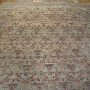 Large area rug featuring a faded botanical pattern in muted beige, blue, and brown on wood flooring.
