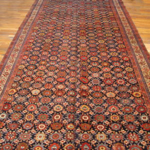 Long runner rug with a navy, red, and gold repeating geometric pattern on light wooden floors.