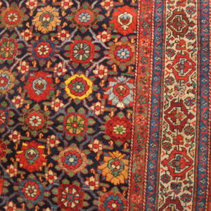 Traditional rug with dense red, blue, and gold floral motifs on a dark field, visible on hardwood floor.