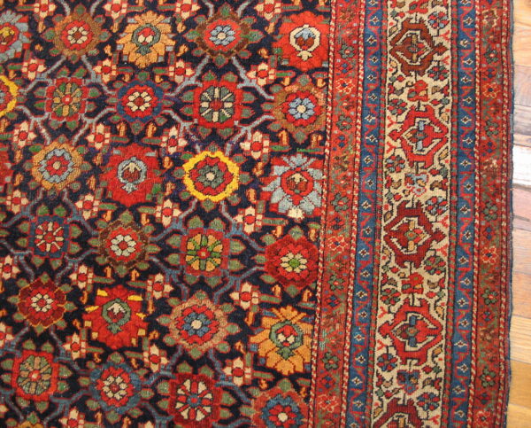 Traditional rug with dense red, blue, and gold floral motifs on a dark field, visible on hardwood floor.