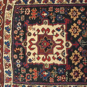 Geometric rug pattern featuring a cream center medallion against a dark blue field with red and gold accents.