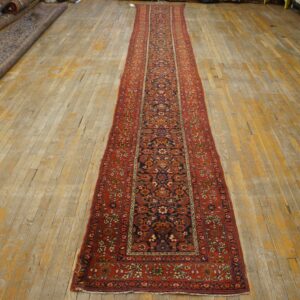 Traditional red border and navy field runner rug on light, distressed wood plank flooring.