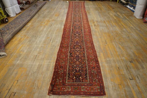 Traditional red border and navy field runner rug on light, distressed wood plank flooring.