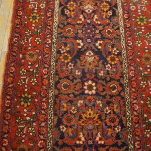 Traditional runner rug in red, navy, and gold floral patterns rests on distressed light wood planks.