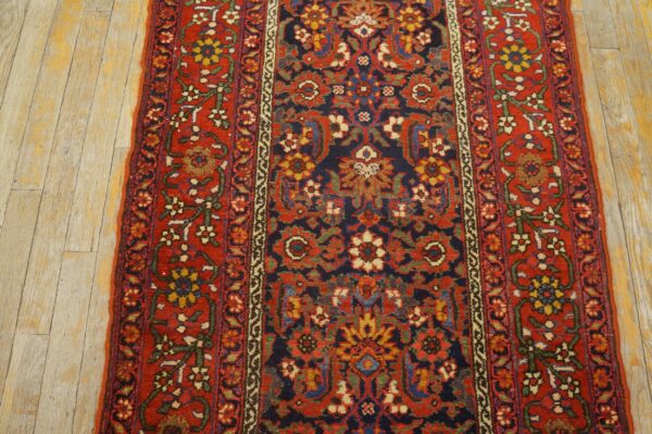 Traditional runner rug in red, navy, and gold floral patterns rests on distressed light wood planks.