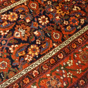 Intricate traditional rug pattern featuring rich red, navy, and colorful floral and geometric details.