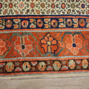 Rust and navy bordered rug with intricate floral motifs and a dense pile resting on gray wood flooring.