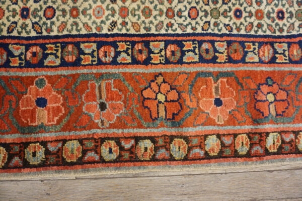 Rust and navy bordered rug with intricate floral motifs and a dense pile resting on gray wood flooring.
