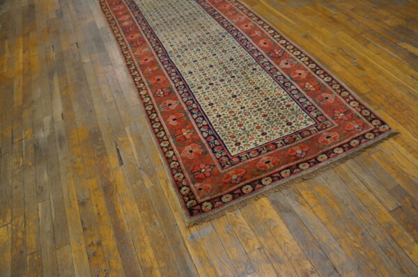 Low-pile runner with rust-red floral borders and a detailed cream field on distressed wood planks.