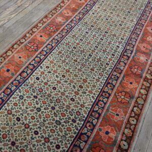 Cream runner rug with a dense floral pattern and wide coral and navy borders on distressed wood floors.