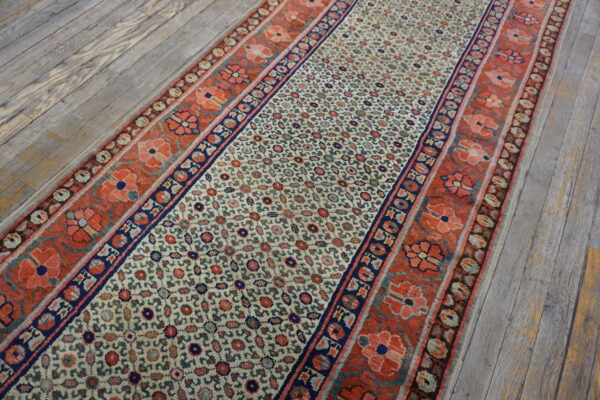 Cream runner rug with a dense floral pattern and wide coral and navy borders on distressed wood floors.