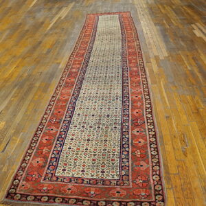 A long traditional runner rug with a cream field and rust borders rests on distressed wood flooring.