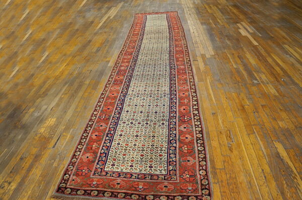 A long traditional runner rug with a cream field and rust borders rests on distressed wood flooring.