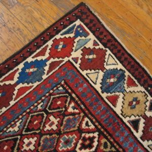 Geometric tribal rug corner in red, blue, black, and cream resting on distressed wood floors.