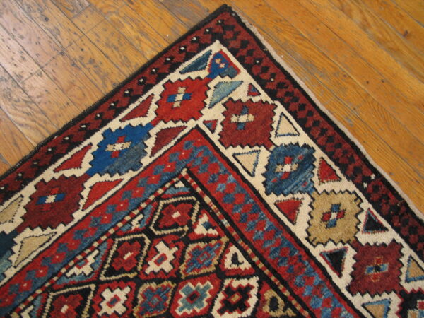 Geometric tribal rug corner in red, blue, black, and cream resting on distressed wood floors.
