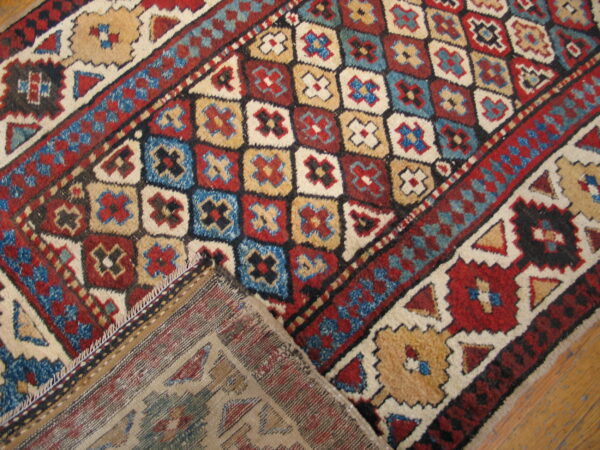 Colorful tribal rug with red, blue, beige, and cream geometric repeating patterns on a wood floor.