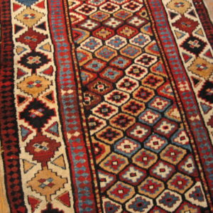 Geometric runner rug with alternating red, blue, and tan diamond medallions on light wood floor.