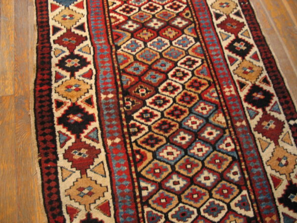 Geometric runner rug with alternating red, blue, and tan diamond medallions on light wood floor.