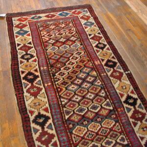 A narrow rug with repeating colorful geometric patterns lies diagonally across light brown plank flooring.