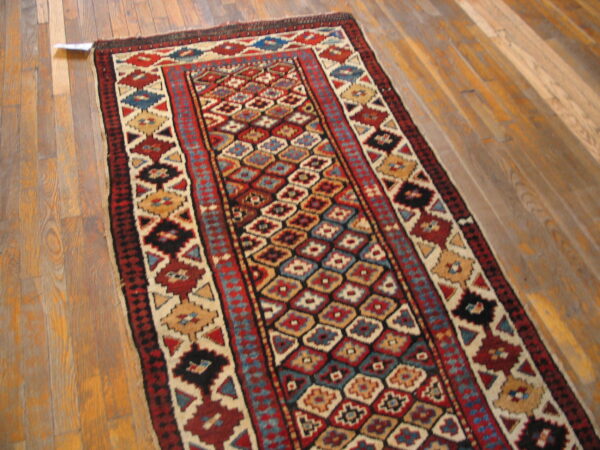 A narrow rug with repeating colorful geometric patterns lies diagonally across light brown plank flooring.