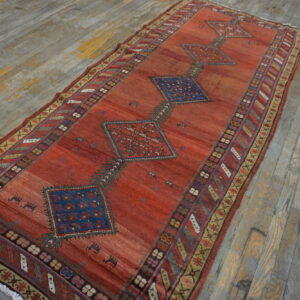 Reddish-orange geometric rug runner with blue diamond medallions resting on distressed wood flooring.