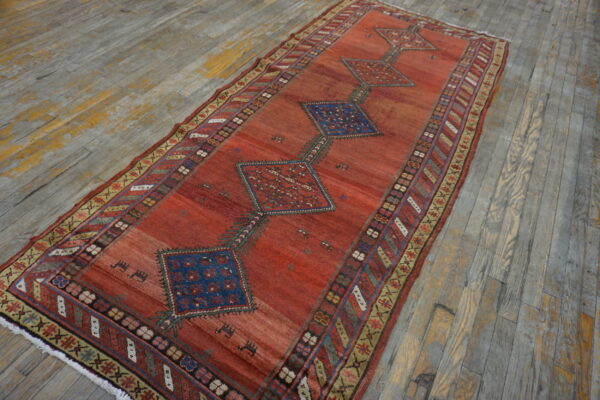 Reddish-orange geometric rug runner with blue diamond medallions resting on distressed wood flooring.
