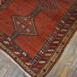 Muted red geometric rug with blue and cream accents lying on rustic gray plank flooring.