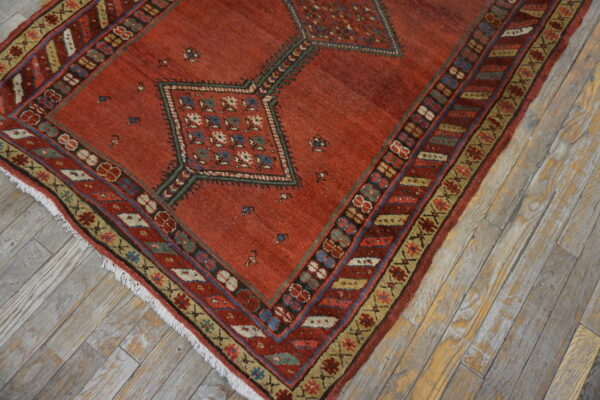 Muted red geometric rug with blue and cream accents lying on rustic gray plank flooring.