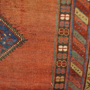 Detailed view of a textured orange rug with a blue medallion corner and multiple geometric borders.