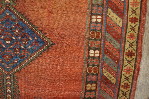 Detailed view of a textured orange rug with a blue medallion corner and multiple geometric borders.