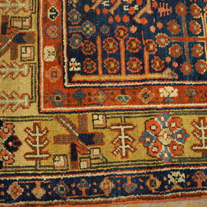 Detailed rug corner featuring a complex navy blue, terracotta, and gold geometric pattern on wood planks.