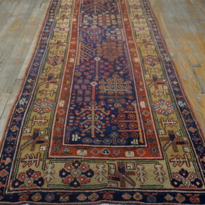 Low-pile geometric runner rug in shades of blue, red, and khaki on worn wood planks.