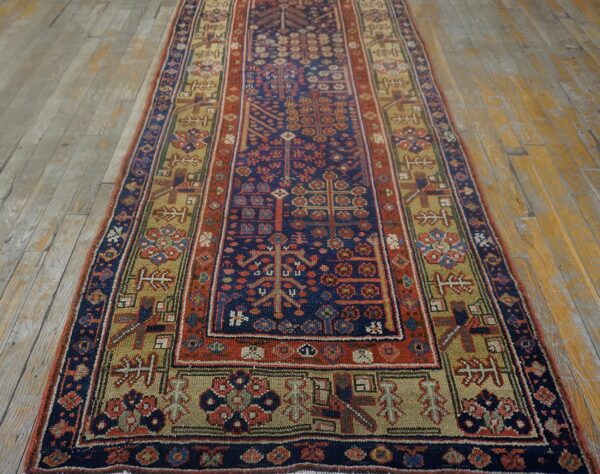 Low-pile geometric runner rug in shades of blue, red, and khaki on worn wood planks.